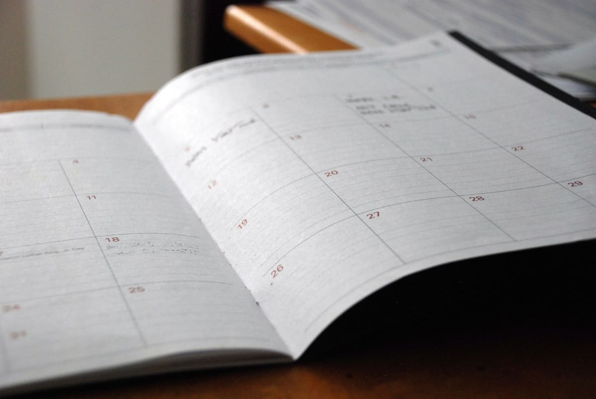 An open monthly planner on a wooden desk, a few dates written in by hand