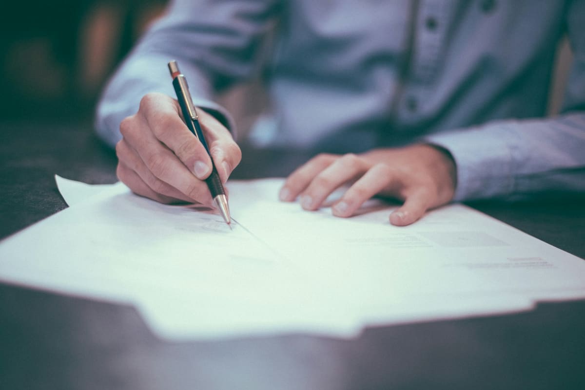 A hand signing a printed document with a ballpoint pen