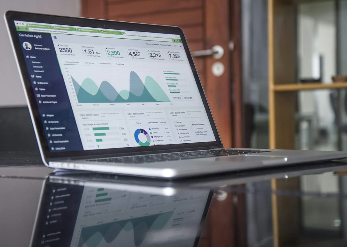 An open laptop on a glossy desk, its screen showing a dashboard of charts and figures