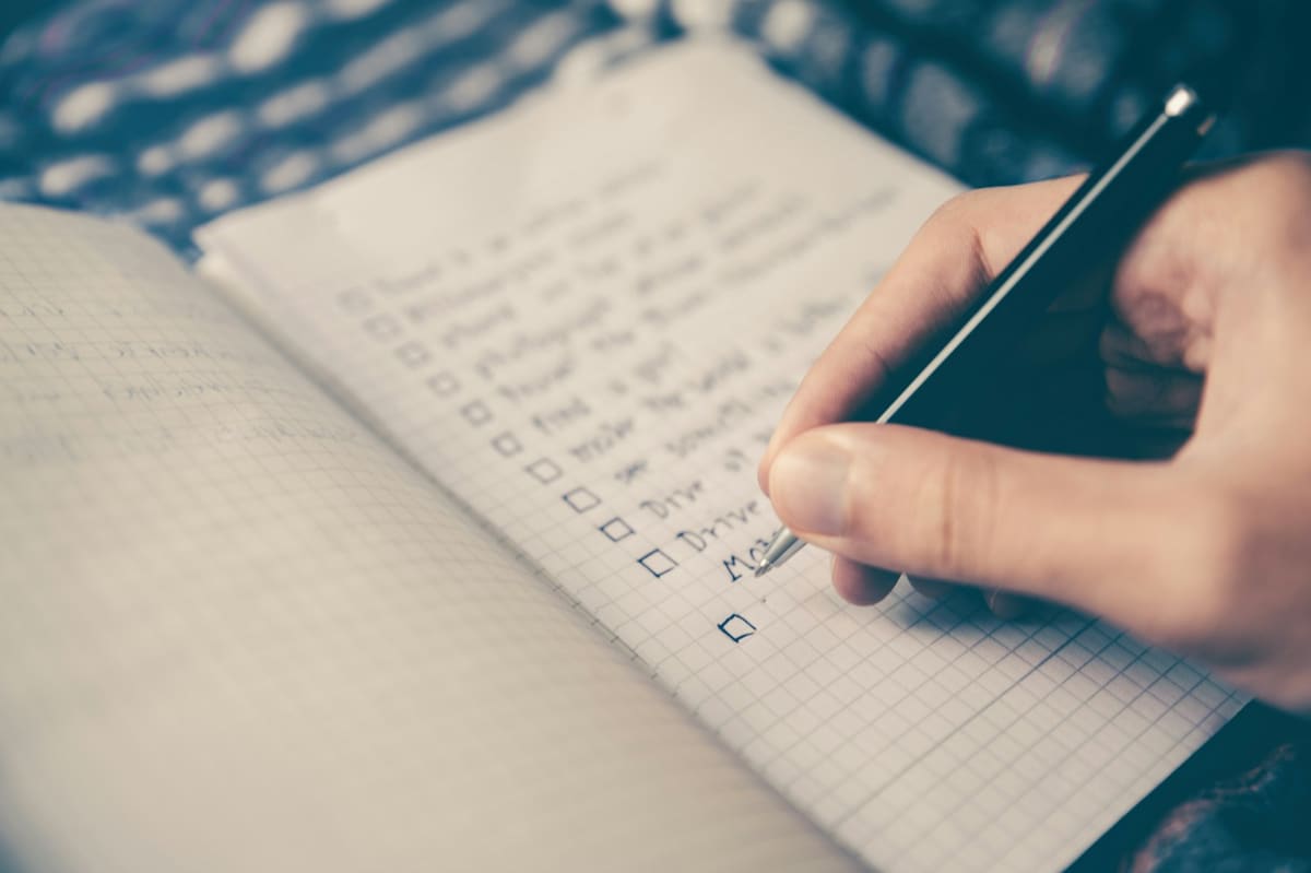 A hand writing a to-do list with tick boxes in an open notebook