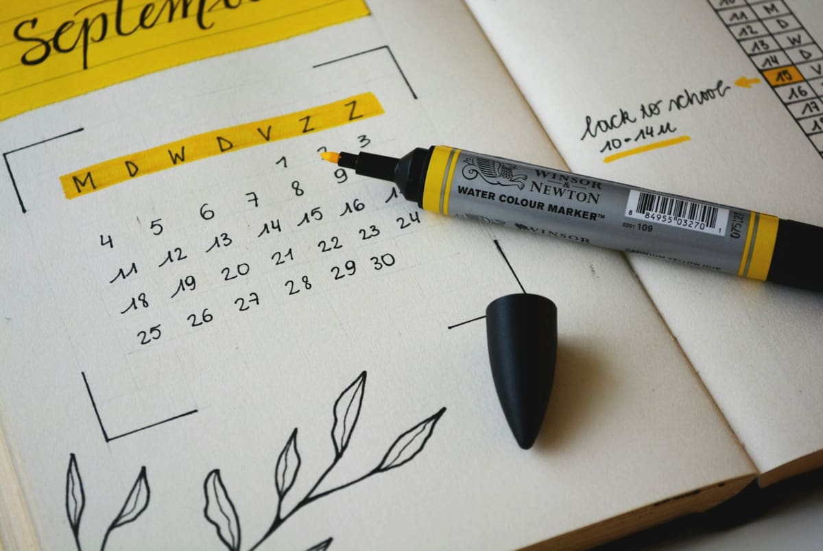 A hand-drawn September calendar in an open notebook, with a yellow marker lying across it