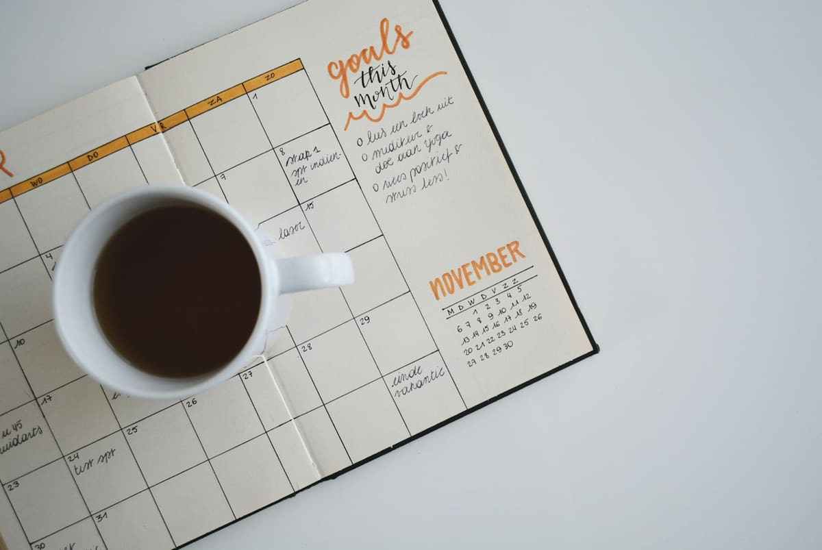 An open planner showing a month’s calendar, with a cup of black coffee resting on the page