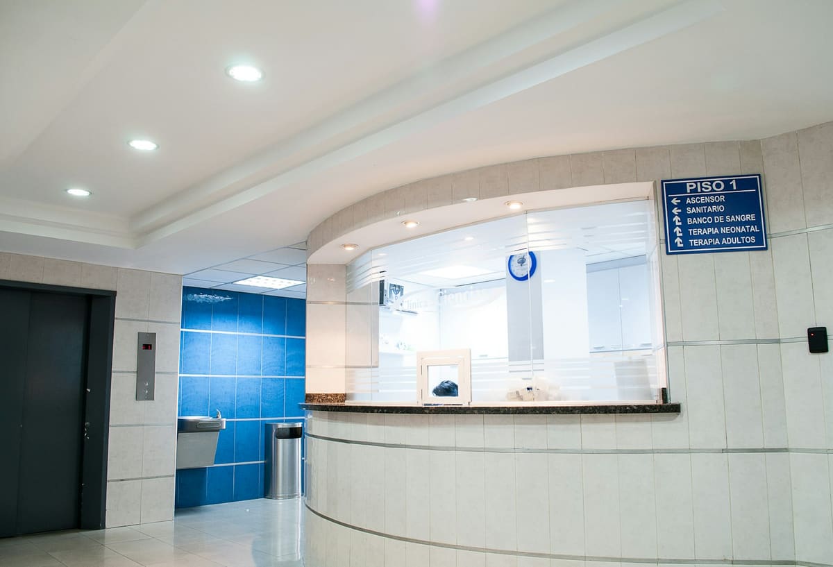 An empty curved reception desk in a brightly lit clinic, a floor directory sign on the wall beside it