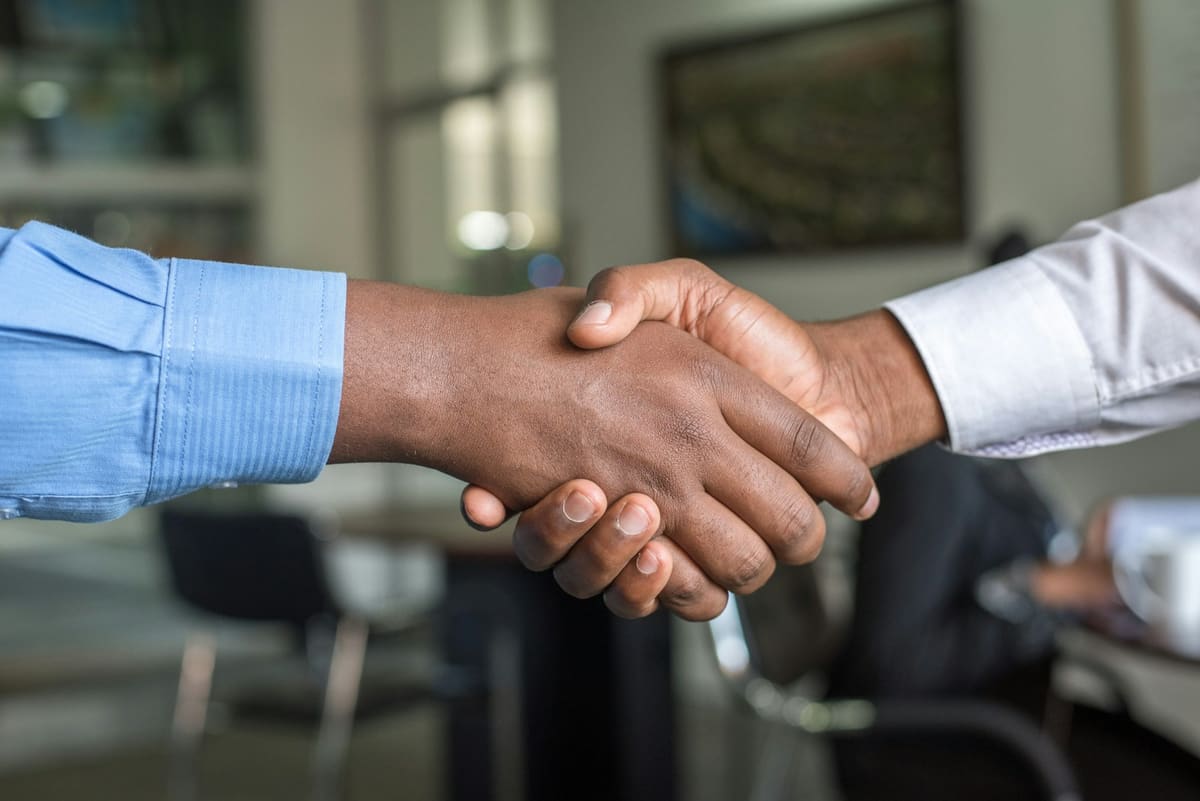 Two people in shirt sleeves shaking hands across a desk in an office