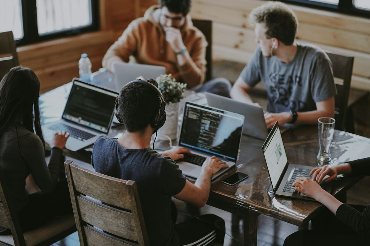 Five people working on laptops around a long wooden table