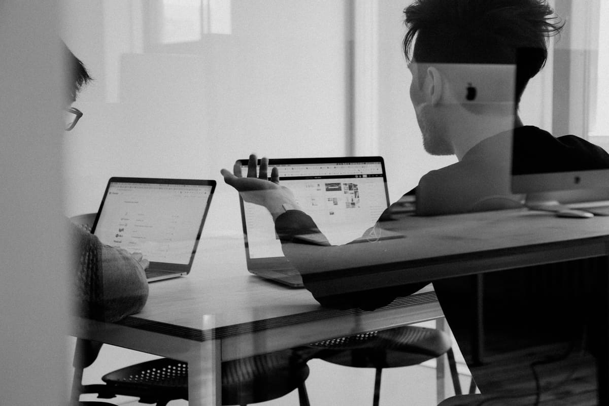 Two people working on laptops at a shared desk, in black and white