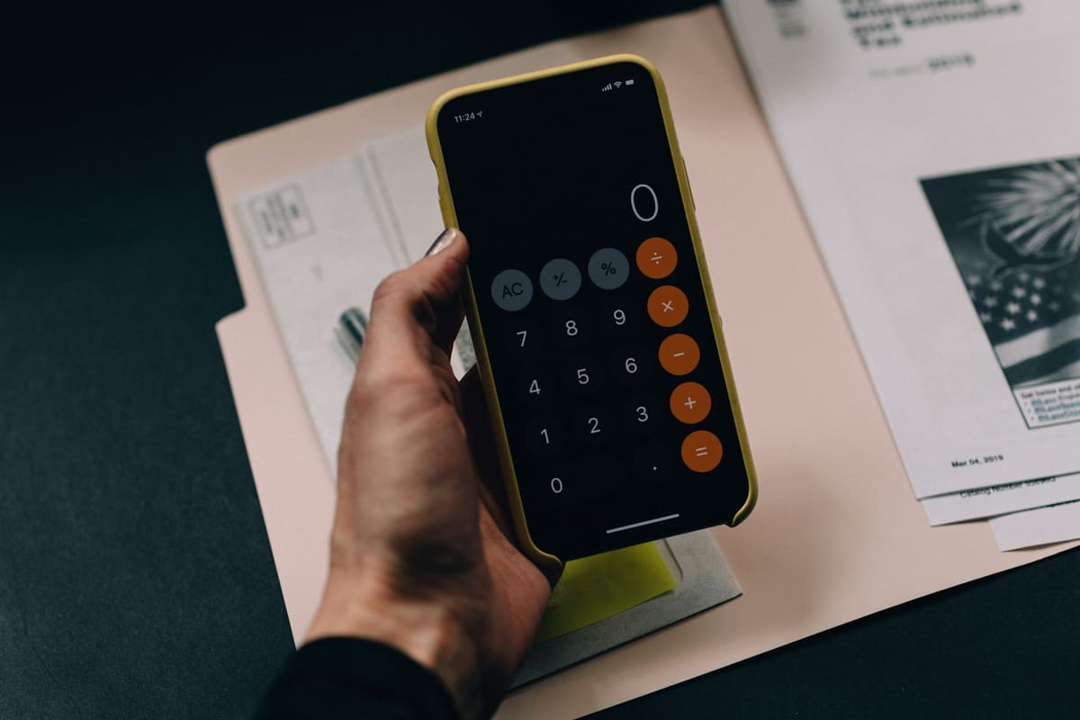 A hand holding a phone with its calculator open over a folder of printed papers
