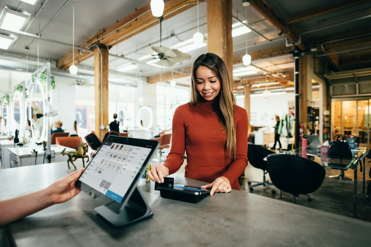 A customer tapping a card on a reader at a shop counter, beside a billing tablet