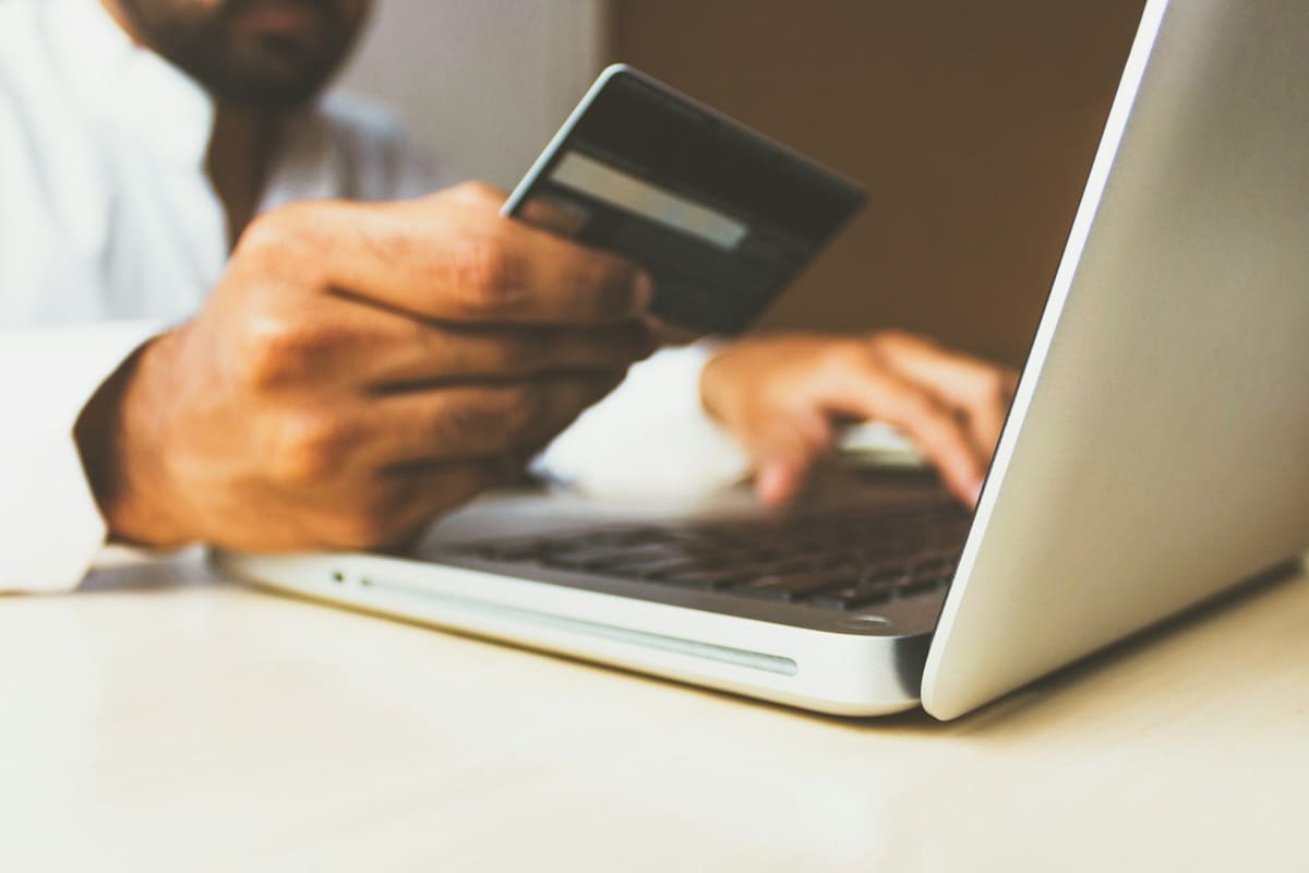 A man holding a bank card in one hand and typing on a laptop with the other