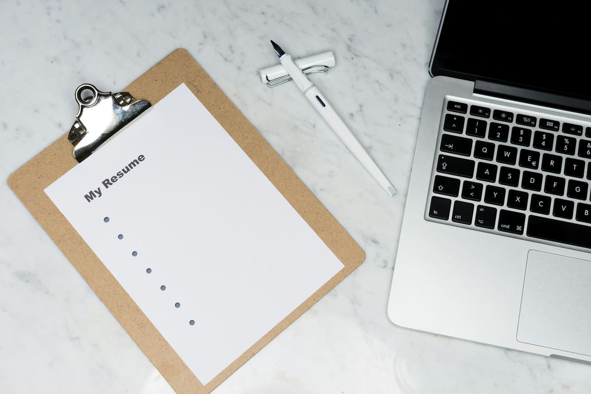 A clipboard holding a page headed My Resume, beside a pen and an open laptop on a marble desk